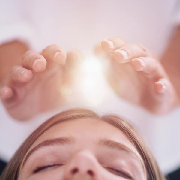 Close up image of relaxed young woman lying with her eyes closed and having Reiki healing treatment in spa center. Energy healing concept.